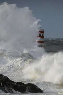 Onda alta a bater num rochedo que tem um farol vermelho.